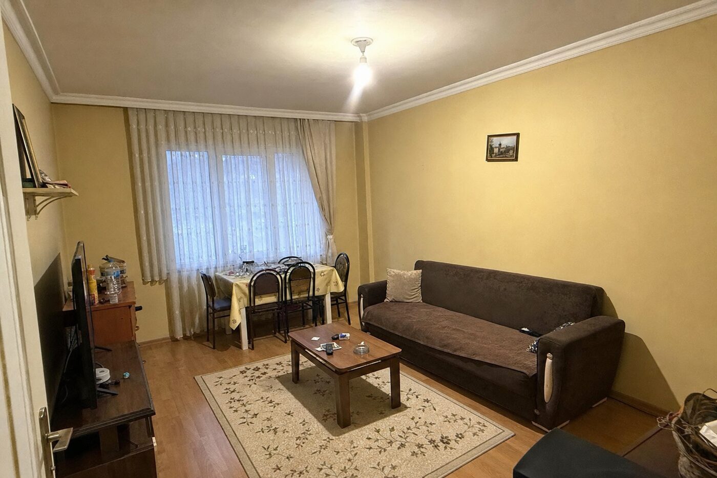ChatGPT ile oda tasarımı öncesi - sıkıcı ve dağınık bir salon, duvara yapışık kahverengi kanepe, küçük halı ve tek tavan lambası